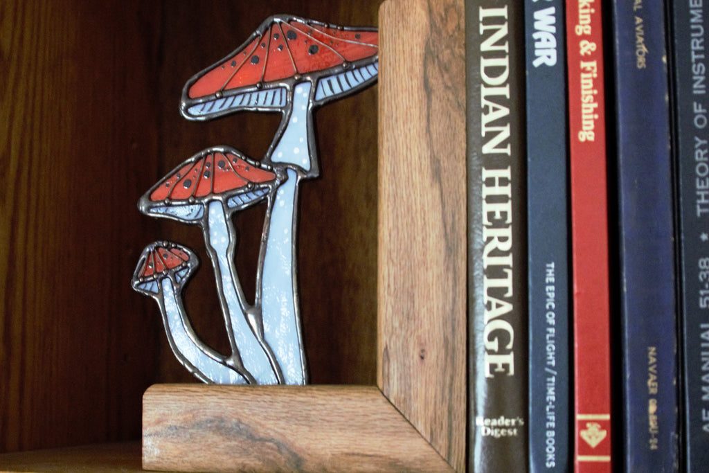 Handmade stained glass mushroom bookend in soft moody blue-grey tones, on a wooden shelf

