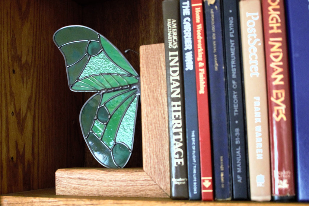 Handmade stained glass butterfly wing bookend in deep jewel tones, displayed on a shelf