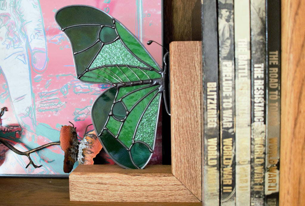 Handmade stained glass butterfly wing bookend in deep jewel tones, displayed on a shelf